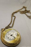 Front and angled views of the Lucerne pendant pocket watch showing the fluted design and white dial with Arabic numerals.