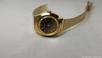 Full angled view showing gold tone case, black dial with applied gold markers, and metal bracelet.