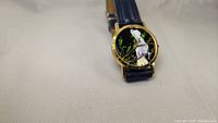 Front angled view of the watch showing the handpainted bird dial and part of navy blue strap.
