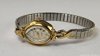 Waltham ladies wristwatch showing gold-tone case, white dial with Arabic numerals, and stainless steel band.