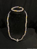 Full view of the blue, yellow, white, red, and orange handmade glass bead necklace and matching bracelet displayed on a black mannequin bust.