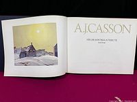 Open book showing title page and painting with text 'A.J. Casson His Life & Works/A Tribute' by Paul Duval, published by Cerebrus/Prentice Hall