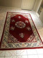 Full view of the red floral area rug laid flat on a white tiled floor. Shows the detailed floral medallion and border.