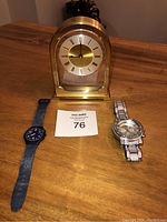 Photo showing the entire lot: one gold-toned Junghans mantle clock, one blue Swatch wristwatch, and one silver-tone Ice Star wristwatch with crystals.