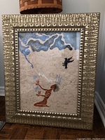 Framed artwork showing a stylized figure, blue and black background elements, with detailed gold decorative frame.