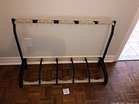 Front view of Konig & Meyer guitar stand with 5 guitar holders, black frame with beige hooks, standing on wood floor.