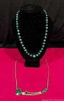 Photo showing both vintage malachite necklaces on black display bust with red background.