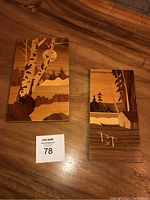 Photo showing two marquetry wooden panels side by side on a wooden surface, with natural landscape scenes inlaid