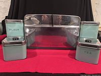Front view of turquoise GSW breadbox with chrome metal finish and four matching canisters, two labeled Flour and Tea, showing wear and scratches.