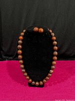 Red jasper necklace displayed on black velvet stand with matching round red jasper earrings on top of stand.