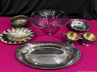 All items arranged on a red cloth background showing silver overlay bowl, silverplated trays, brass bowl, and silverplated sugar and creamer set.