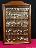 Full view of wooden display case holding over 50 souvenir spoons arranged in rows