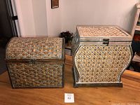 Pair of two wicker weave lidded storage containers with latch closures on wood surface.