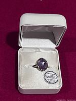 Front view of the silver ring featuring an oval purple Swarovski crystal in a white cushioned box with Swarovski label