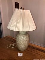 Full view of the vintage ceramic table lamp with crackle glaze and white pleated shade on wooden surface.