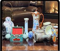 Full view on table of multiple Asian porcelain and pottery decorative pieces including teapots, vases, cups, and figurines.