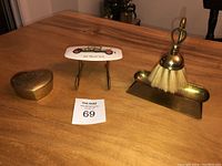 Photo showing all three items: brass crumb catcher with brush, heart-shaped trinket box, and miniature brass hanger with porcelain top with vintage car design.