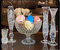 Crystal bowl, bud vases, and decorative eggs arranged on table including background details