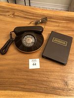 Full view of vintage brown rotary telephone and accompanying black telephone and address register book on a wooden surface.