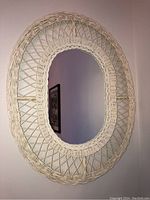 Full view of oval wicker-framed mirror on wall showing overall design and condition.