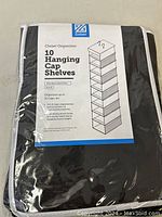 Photo of front label showing brand, product name, use for organizing up to 10 caps, black color, and features such as metal hooks, washable polyester fabric.