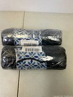 Two rolled black beach towels inside carrying cases with a blue and white geometric pattern and black drawstrings.