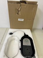 Photo of 30A surge protector showing black device with clear protective cover, resting on table with its box behind.