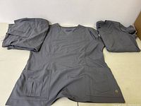 Set of three new gray medical smocks laid flat, showing front design and pockets.