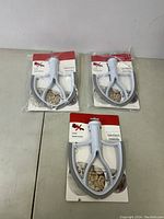 Three new kitchen mixer scrapers in packaging laid out on a table, showing front of packages with red and white backing card.