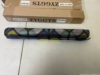 Three rolls of window stained glass film in brown cardboard boxes placed on a white surface, one roll partially unrolled displaying geometric colored pattern.