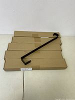 Four black metal wreath hook hangers stacked on four rectangular cardboard boxes.