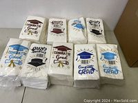 Nine packs of new, sealed graduation party napkins with different congratulatory designs and colors including blue, burgundy, black, and gold.