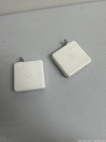 Two white Apple 85W power adapters side by side on a table surface, showing the Apple logo on each charger and foldable plugs.