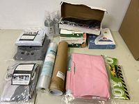 Overview of the lot showing multiple kitchen and home items including linens, cleaning sprays, boxed goods, and wrapped fabric rolls.