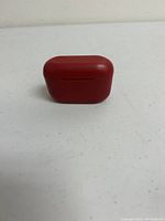 Closed red charging case shown from front view on white surface.