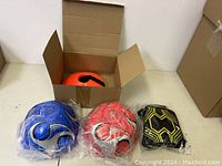 Blue and red soccer balls, goalkeeper gloves, and cones in box on table
