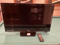 Front view of 30 inch Magnavox flat screen TV with remote control placed on the base to the right side.