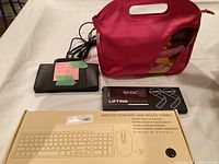 Photo showing black Phillips dictation foot pedal, wireless keyboard and mouse combo in box, SKDK lifting straps in box, and pink carrying case with curling irons.