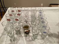 Photo showing 24 assorted beer glasses on a white surface, including brands Guinness, Labatt Blue, Molson Canadian, Red Stripe, and Heineken.