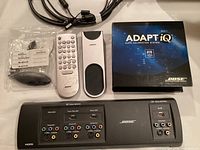 Photo of Bose Adapt-iQ system items including video enhancer, remotes, cables, and box laid out on a flat surface.