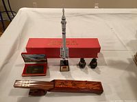 Photo showing wooden chopsticks with carved holder, two small figurines, and a China space rocket model with its original box on a table.