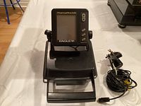 Photo of an Eagle SupraPro I.D. portable fish finder on its stand with a wired transducer beside it.