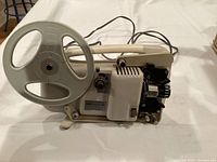 Front angle showing Holbeck 8mm film projector with reel attached, power cord, mechanical controls and ventilation housing.