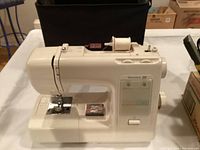White Kenmore 20 sewing machine on a table with black carrying case behind it.