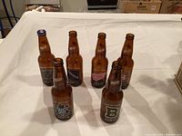 Photo showing six empty Labatt Blue beer bottles with different vintage and original labels on a white surface.