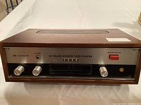 Front view of Sharp B-Track stereo tape player showing wood case, volume, tone, balance knobs, and four program selector buttons above tape slot.