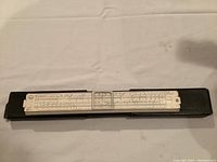 Top-down view of the slide rule fully extended on a white surface with the black protective case beneath it.