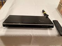 Front and top view of the black Toshiba DVD player with visible surface scratches and remote beside it.