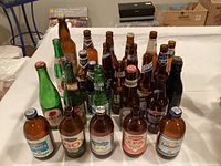 Photo showing 26 vintage used beer bottles in various colors and brands, mostly brown and green glass bottles with labels and caps intact.