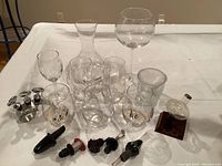 Photo of a table displaying multiple glass wine glasses, a carafe, various bottle stoppers, and a glass wine aerator with wooden base.